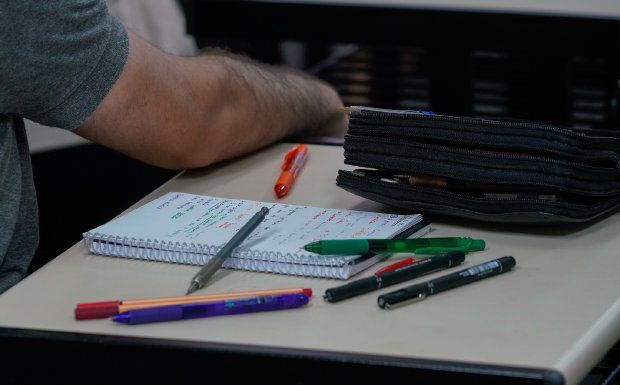 caderno, lápis e canetas em cima de mesa com homem ao lado