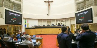 plenário da alesc, com uma cruz religiosa no alto e deputados em pé e sentados, as telas mostram a votação do pl que prevê notebooks para professores da rede pública estadual de Santa Catarina