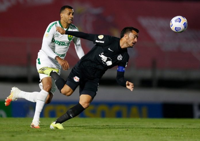 jogador do bragantino quase caindo correndo atrás da bola seguido por adversário