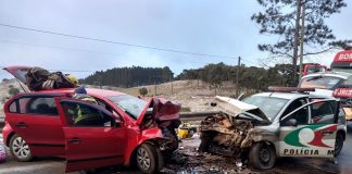 A foto mostra um veículo vermelho de frente para uma viatura da polícia militar, os dois veículos têm a parte da frente destruídas após uma colisão frontal, que deixou um policial morto e outros feridos em ANita Garibaldi. A pista tinha gelo no momento do acidente.