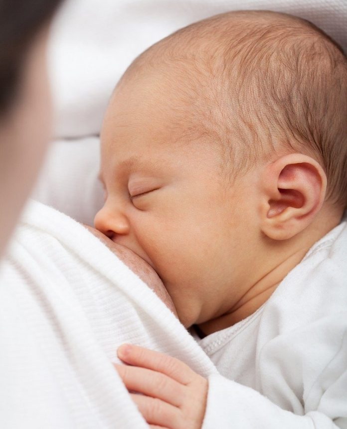 Um bebê aparece de olhos fechados mamando. A campanha Agosto Dourado promove a amamentação e a importância do aleitamento materno.