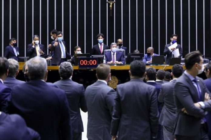 Deputados sentados no plenário de frente para outros deputados, que aparecem de costas na foto, todos vestem ternos. Os deputados aprovaram o texto base da reforma eleitoral, que entre alguns pontos votou o distritão e as coligações.