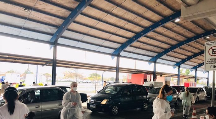 Ponto de vacinação drive-thru na capital, no aeroporto, com uma fila de carros e profissionais de saúde em pé e sentado em uma mesa. Florianópolis terá o passaporte de vacinação para entrada em hotéis, bares e eventos.