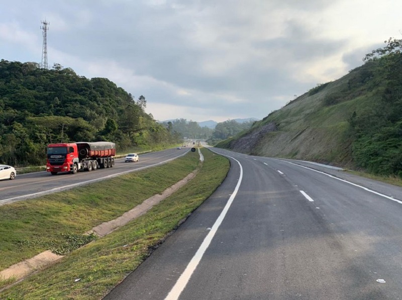 Trecho da BR-470 em SC, com uma pista cinza com marcas brancas à direita, uma parte com grama ao centro e à esquerda outra pista, com carros e um caminhão. O governador Carlos Moisés envia à Alesc o PL para doação de mais R$115 milhões para obras em rodovias federais.