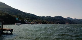 costa da lagoa vista da altura da água com montanhas e algumas casas em meio à vegetação