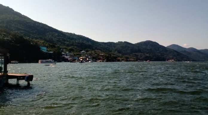 costa da lagoa vista da altura da água com montanhas e algumas casas em meio à vegetação