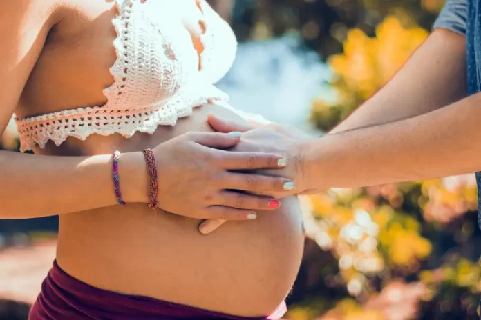 homem coloca as mãos sobre barriga de grávida em ambiente externo com flores