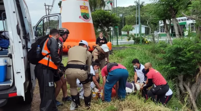 equipes de resgate retirando corpo ao lado de barrando com árvores - Motociclista morre em frente ao posto policial da SC-401