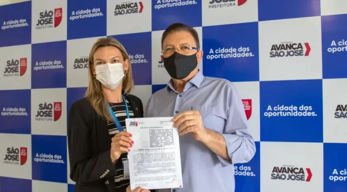 Lagoa de Potecas: área é cedida à Casan para construção de estação de tratamento |ávila e maas posam para foto segurando documento, ambos de máscaras, painel da prefeitura de são josé ao fundo